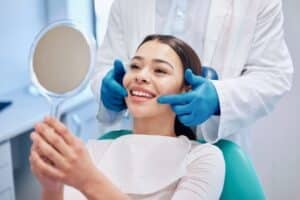 NYC woman smiles looking into the mirror at her teeth after a pleasant dental experience.