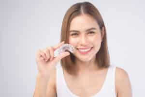 Mixed race patient holds up her Invisalign aligner, pleased with how unpainful the process is.