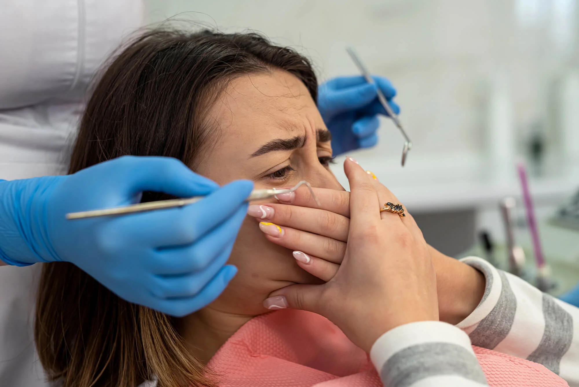 Woman experiencing dental anxiety in NYC before procedure, covering mouth with hands in panic over dental pain.